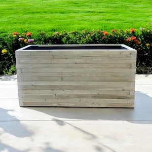 May include: A rectangular wooden planter box with a light grey finish. The planter is made of horizontal slats of wood and has a black liner inside.