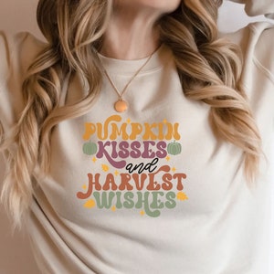 May include: A beige sweatshirt with the text "Pumpkin Kisses and Harvest Wishes" in a retro font with autumn-themed graphics.