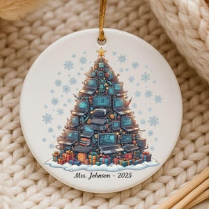 May include: A white ceramic Christmas ornament with a gold string. The ornament features a Christmas tree design made of computers, keyboards, and gifts. The text "Mrs. Johnson - 2025" is printed at the bottom. Blue snowflakes are scattered around the tree.