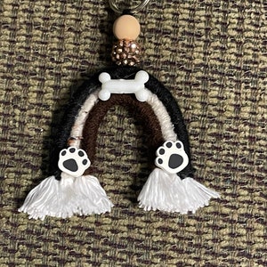 May include: A rainbow-colored yarn keychain with a white bone charm and paw print charms. The keychain has white tassels and a silver key ring.