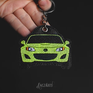 Può includere: Un portachiavi per auto verde lime con dettagli neri. Il portachiavi è realizzato in tessuto e ha un retro in pelle nera. Il portachiavi è attaccato a un portachiavi in metallo argentato.