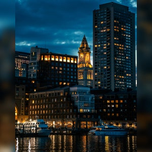 Pode incluir: Vista noturna de um horizonte urbano com vários edifícios altos, incluindo uma torre com um relógio, iluminados por postes de luz. Os edifícios são refletidos na água abaixo.