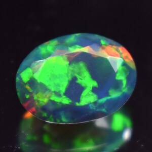 May include: A green, blue, and red opal gemstone with a smooth, oval shape.