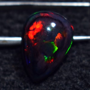 May include: A black opal gemstone with red, green, and orange flashes of color. The gemstone is cut in a teardrop shape.
