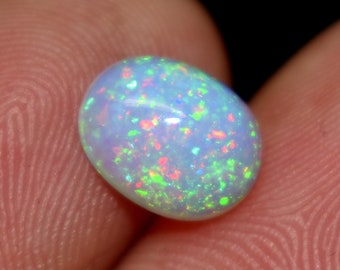 Puede incluir: Una piedra preciosa de ópalo blanco con una base azul claro y destellos iridiscentes de verde, rojo y naranja.