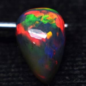 Könnte beinhalten: Ein tropfenförmiger schwarzer Opal-Edelstein mit einem dunkelgrauen Körper und Blitzen von Rot, Grün, Blau und Gelb.