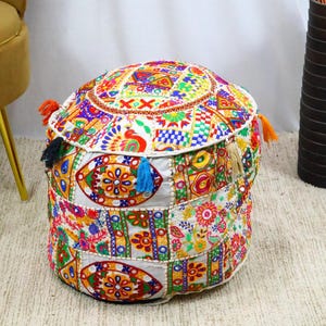 Könnte beinhalten: Ein runder, farbenfroher Pouf mit Patchwork-Design. Der Pouf weist eine lebendige Mischung aus Mustern auf, darunter florale und geometrische Motive, in Rot-, Gelb-, Blau- und Grüntönen. Er hat dekorative Quasten in verschiedenen Farben und wird wahrscheinlich zum Sitzen oder als Fußstütze verwendet.