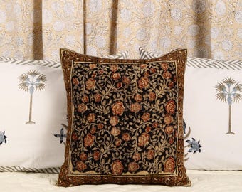 May include: A black and brown patterned throw pillow with a floral design. The pillow is sitting on a white bedspread with a floral pattern.