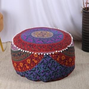 May include: Round, patterned floor pouf with a vibrant mandala design. The pouf features a mix of red, purple, and blue hues with floral and geometric patterns. White pom-pom trim accents the edges. A decorative accent for any living space.