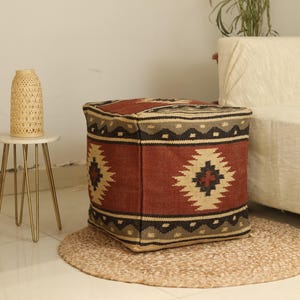 Puede incluir: Un puf cuadrado de color rojo, marr&oacute;n y beige con un patr&oacute;n tejido. El puf est&aacute; sobre una alfombra tejida beige.