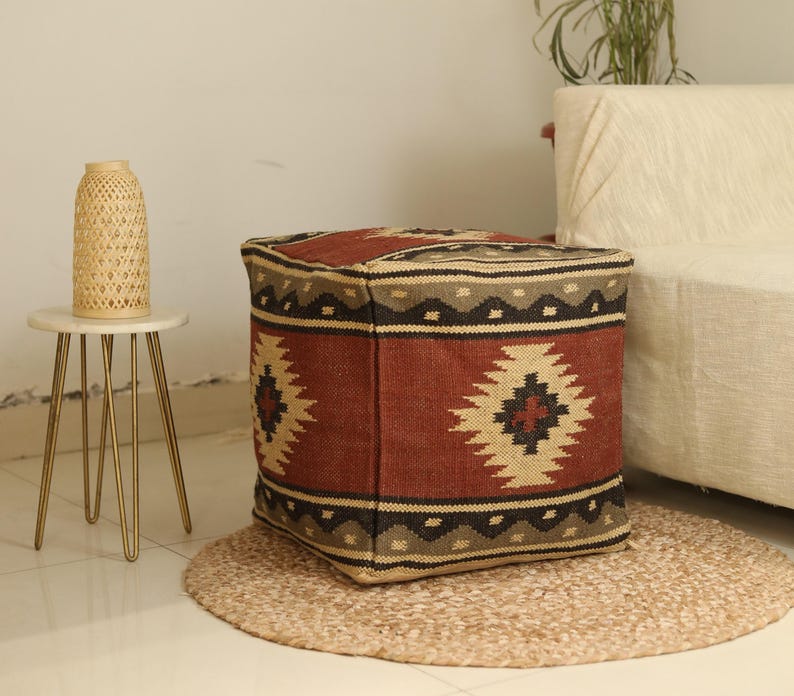 Puede incluir: Un puf cuadrado de color rojo, marr&oacute;n y beige con un patr&oacute;n tejido. El puf est&aacute; sobre una alfombra tejida beige.