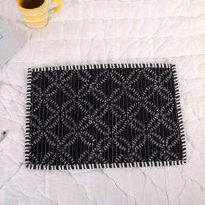 May include: A black and white patterned laptop sleeve. The sleeve has a geometric design with vertical and diagonal lines. The edges are trimmed with a white and black striped border. A yellow mug with black stripes is visible in the background.