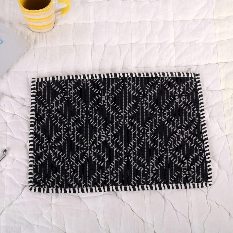 May include: A black and white patterned laptop sleeve. The sleeve has a geometric design with vertical and diagonal lines. The edges are trimmed with a white and black striped border. A yellow mug with black stripes is visible in the background.