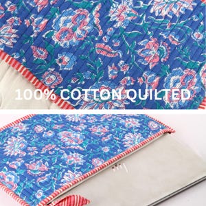 May include: A blue quilted cotton laptop sleeve with a floral pattern in pink and white. The sleeve has a red and white striped border and the text "100% COTTON QUILTED".
