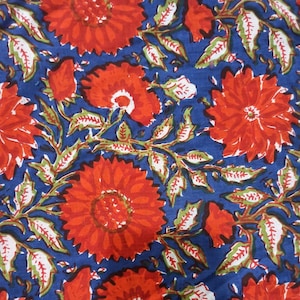 May include: Close-up of a fabric with a floral pattern. The design features large, vibrant red flowers with intricate details, set against a deep blue background. Green and white leaves and stems intertwine, creating a lively and colorful textile.