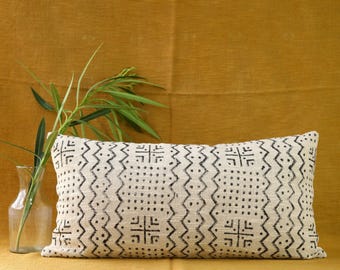 May include: A white rectangular pillow with a black geometric pattern. The pillow is on a yellow surface with a green plant in the background.