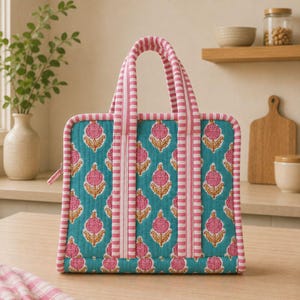 Könnte beinhalten: Eine quadratische, gesteppte Tragetasche mit türkisfarbenem Hintergrund und einem sich wiederholenden Blumenmuster in Pink und Gelb. Die Tasche hat zwei Tragegriffe und Kantenbesatz aus rosa-weiß gestreiftem Stoff sowie einen Reißverschluss.