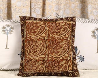 May include: A brown and cream patterned throw pillow with a dark brown border. The pillow is made of a soft, textured fabric and features a paisley design.