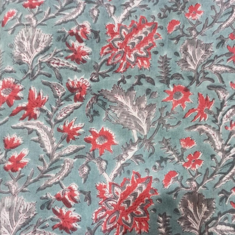 May include: A close-up of a fabric with a floral pattern. The fabric has a teal background with red and gray floral designs. The flowers are of various sizes and shapes, with detailed leaves and stems.