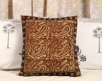 May include: A brown and cream patterned throw pillow with a dark brown border. The pillow is made of a soft, textured fabric and features a paisley design.