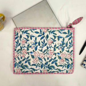 May include: A white laptop sleeve with a floral pattern of pink flowers and blue leaves. The sleeve has a pink and white striped border and a matching zipper pull. A laptop is partially visible inside.