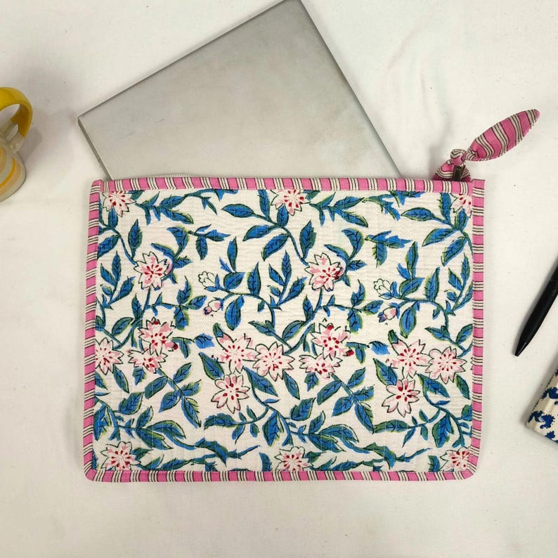 May include: A white laptop sleeve with a floral pattern of pink flowers and blue leaves. The sleeve has a pink and white striped border and a matching zipper pull. A laptop is partially visible inside.