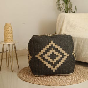Puede incluir: Un puf cuadrado negro y beige con un dise&ntilde;o geom&eacute;trico. El puf est&aacute; sobre una alfombra beige.