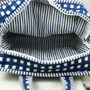 May include: Open view of a blue and white quilted tote bag. The exterior features a checkered pattern, while the interior lining has vertical stripes. The bag has a zipper closure and two handles.