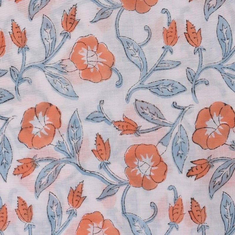 May include: White fabric with a repeating floral pattern. The design features orange flowers, light blue leaves, and orange buds on stems. The pattern is evenly spaced across the fabric.