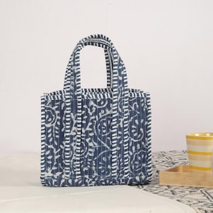 Peut inclure: Un petit sac fourre-tout matelass&eacute; avec un motif floral bleu et blanc. Le sac a deux poign&eacute;es et est fait d'un tissu doux et textur&eacute;. Le sac mesure environ 25 cm de haut et 20 cm de large.