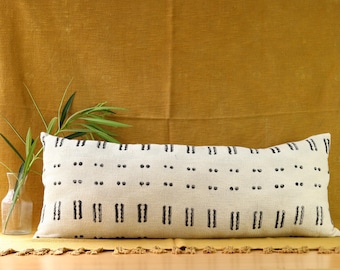 Puede incluir: Una almohada lumbar blanca con un patrón geométrico negro. La almohada está sobre una superficie amarilla.