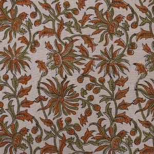 May include: Cream-colored fabric with a repeating floral pattern. The design features large, stylized flowers in shades of orange and brown, with green leaves and stems. The overall aesthetic is reminiscent of traditional block printing.