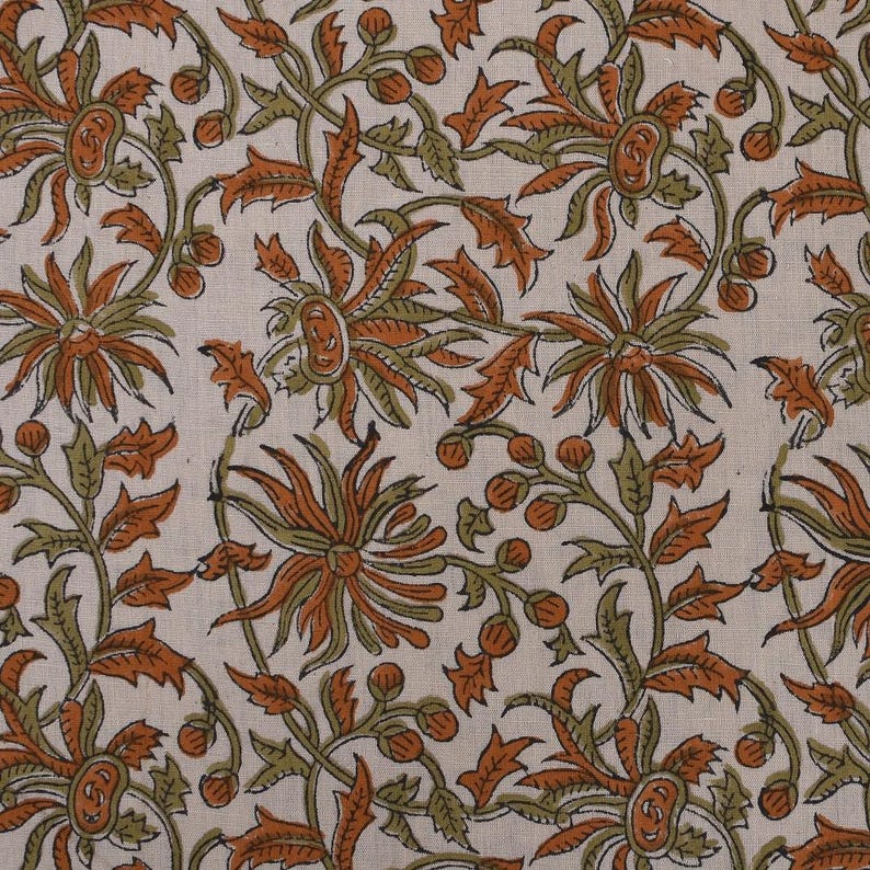 May include: Cream-colored fabric with a repeating floral pattern. The design features large, stylized flowers in shades of orange and brown, with green leaves and stems. The overall aesthetic is reminiscent of traditional block printing.