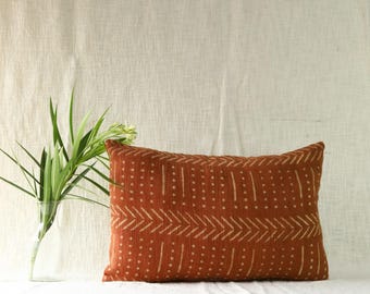 May include: A rectangular throw pillow in a deep burnt orange color featuring a repeating pattern of vertical dotted lines and horizontal chevron arrows in a light cream color. The pillow has a textured fabric appearance and a rectangular shape.