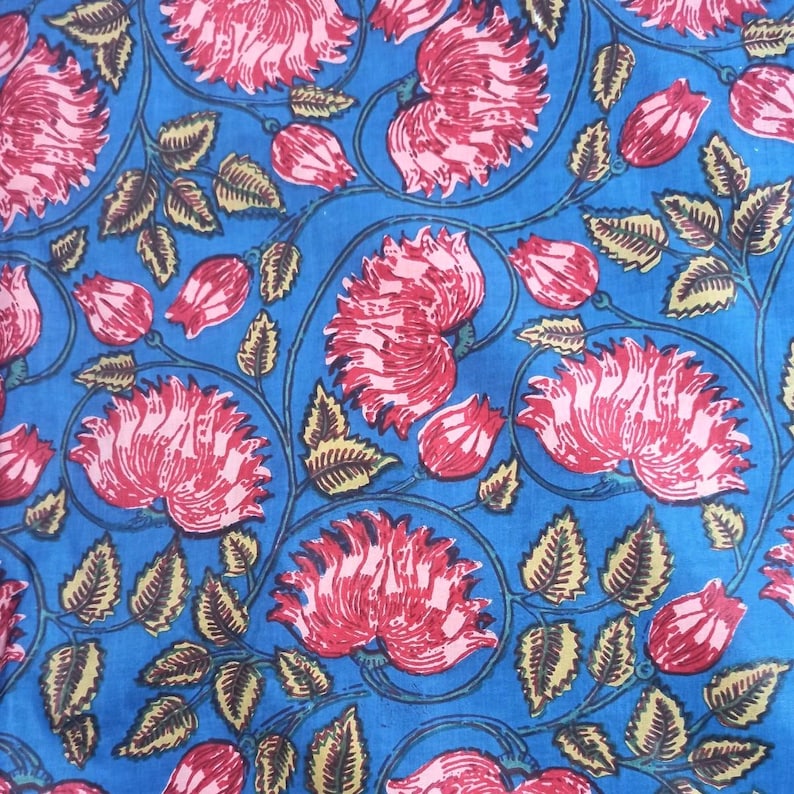 May include: A vibrant blue fabric with a repeating floral pattern. Large, stylized red flowers with pink centers are interspersed with green leaves and stems. The design creates a bold, eye-catching textile.