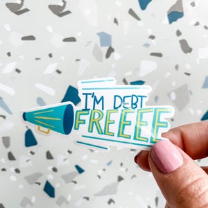 Hand holding sticker that says i'm debt free with a megaphone for money goals and paid off celebrations