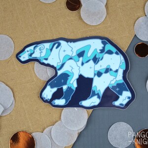 May include: A blue and white polar bear sticker with a starry night sky design. The sticker is on a brown background with white and gold confetti.