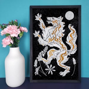 Könnte beinhalten: Ein schwarzer gerahmter Druck eines weißen Wolfes mit goldenen Akzenten, der auf seinen Hinterbeinen steht, mit offenem Maul, vor einem schwarzen Hintergrund mit einem weißen Mond und weißen Blumen.