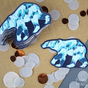May include: A stack of blue and white polar bear stickers with a swirling, abstract design. The stickers are on a brown surface with white and copper confetti.