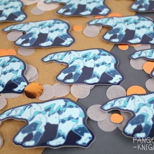 May include: A set of colorful polar bear stickers with a blue, green, and white abstract design. The stickers are on a brown and gray surface with confetti.