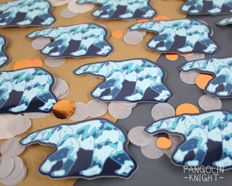 May include: A set of colorful polar bear stickers with a blue, green, and white abstract design. The stickers are on a brown and gray surface with confetti.