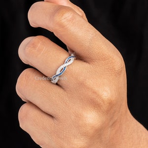 May include: A silver band ring with a twisted design. The ring is set with small blue and white gemstones.
