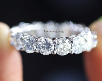 May include: A silver eternity band with a row of round, clear diamonds. The band is held up by a finger with green nail polish.
