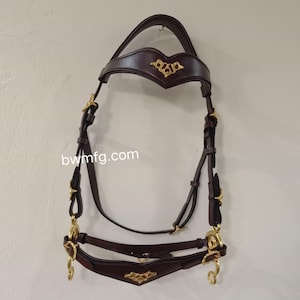 Peut inclure: Une bride de cheval en cuir marron foncé avec des éléments dorés. La bride présente des ornements dorés sur le frontal et la muserolle. Le site web bwmfg.com est imprimé sur l'image.
