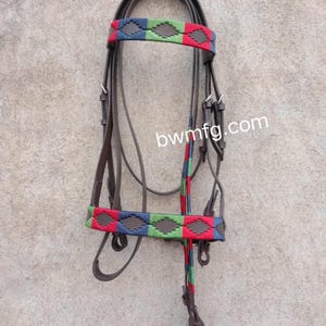 Puede incluir: Una brida de cuero marrón para caballo con una frontalera y muserola que presentan un patrón de diamantes tejido en rojo, verde y azul. La brida incluye hebillas y herrajes de metal plateado, con el texto bwmfg.com visible en el centro.