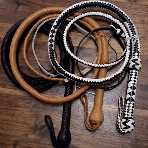 Può includere: Tre fruste in pelle intrecciata avvolte insieme. Una frusta presenta un motivo a rombi bianco e nero, un'altra è color cuoio tinta unita e la terza è marrone scuro tinta unita. Ogni frusta include un manico intrecciato, un cinturino e un nodo.