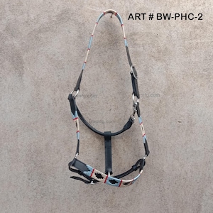 Pode incluir: Um cabresto de cavalo de couro preto com um design de corda trançada branca, azul e vermelha. O cabresto tem uma fivela de metal e um anel de metal. ART # BW-PHC-2