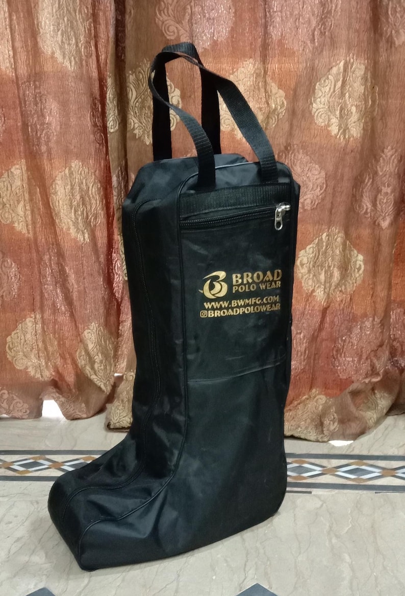 May include: A black boot bag with two top handles and a zippered front pocket. The bag features the gold-colored text Broad Polo Wear, the website www.bwmfg.com, and the social media handle @broadpolowear printed on the front surface.