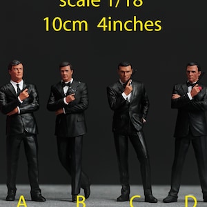 May include: Four black and white figurines of men in suits, standing in a row. The men are holding guns and are posed in different action poses. A pink ruler is in the background for scale. The text "scale 1/18 10cm 4inches" is above the figurines.