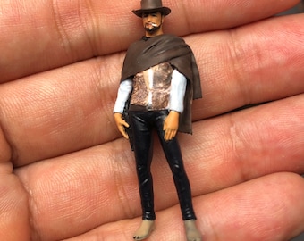 May include: A 1/64 scale figurine of a man wearing a brown hat, a brown poncho, a white shirt, and black pants. The figurine is 1.1 inches tall.